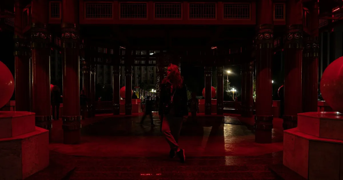 A woman in red lingerie stepping back toward a doorway, candlelight flickering, a man reaching after her