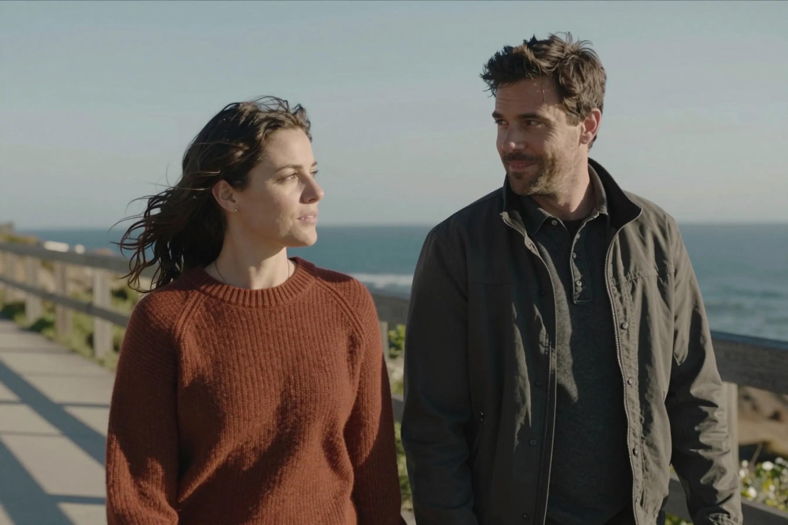 A woman in her late 20s and a man in his late 20s walking together along a coastal path