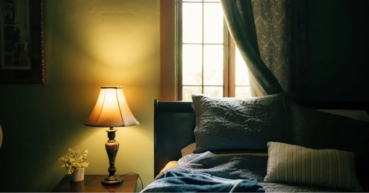 A dim bedroom set for a slow night: warm lamp glow, silk sheets, a record player on the nightstand