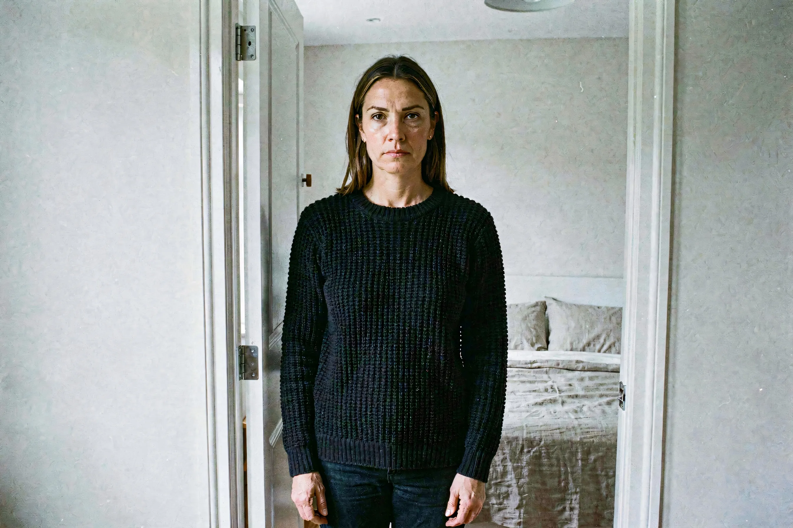 A woman in a dark knit sweater standing beside a doorway in morning light