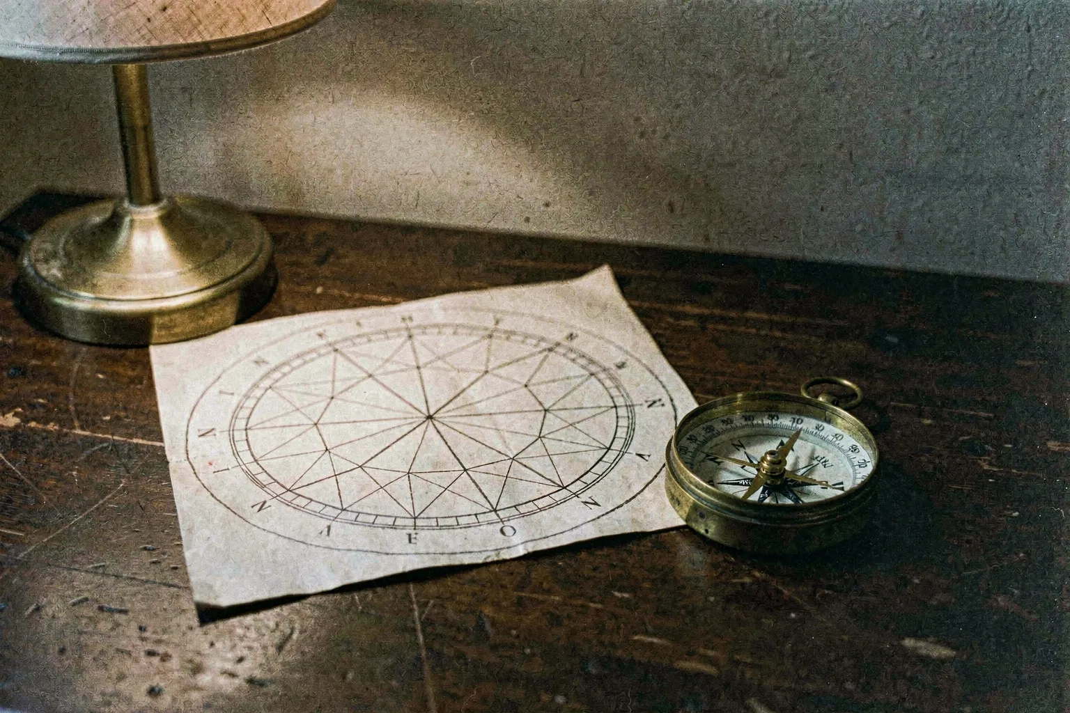 An elegant astrological chart wheel resting on a dark wood table beside a vintage compass and brass instruments, softly illuminated