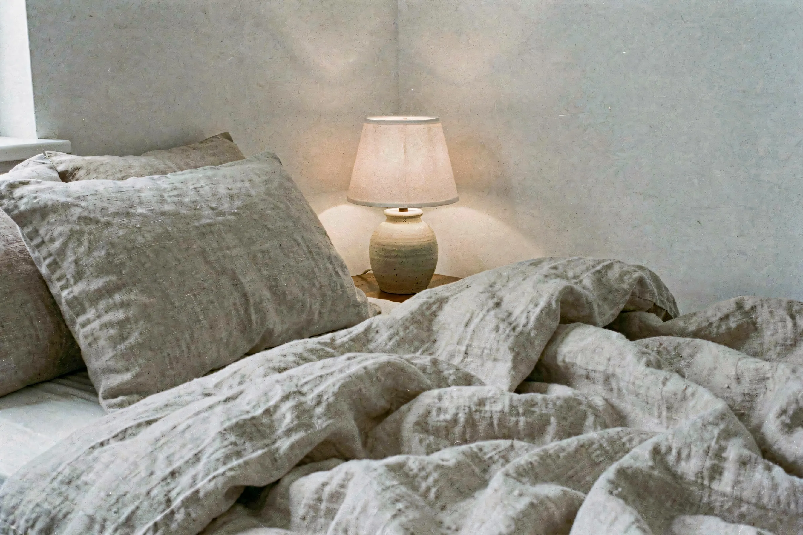 Warm amber lamp glow casting soft shadows across textured linen sheets and pillows in a serene bedroom