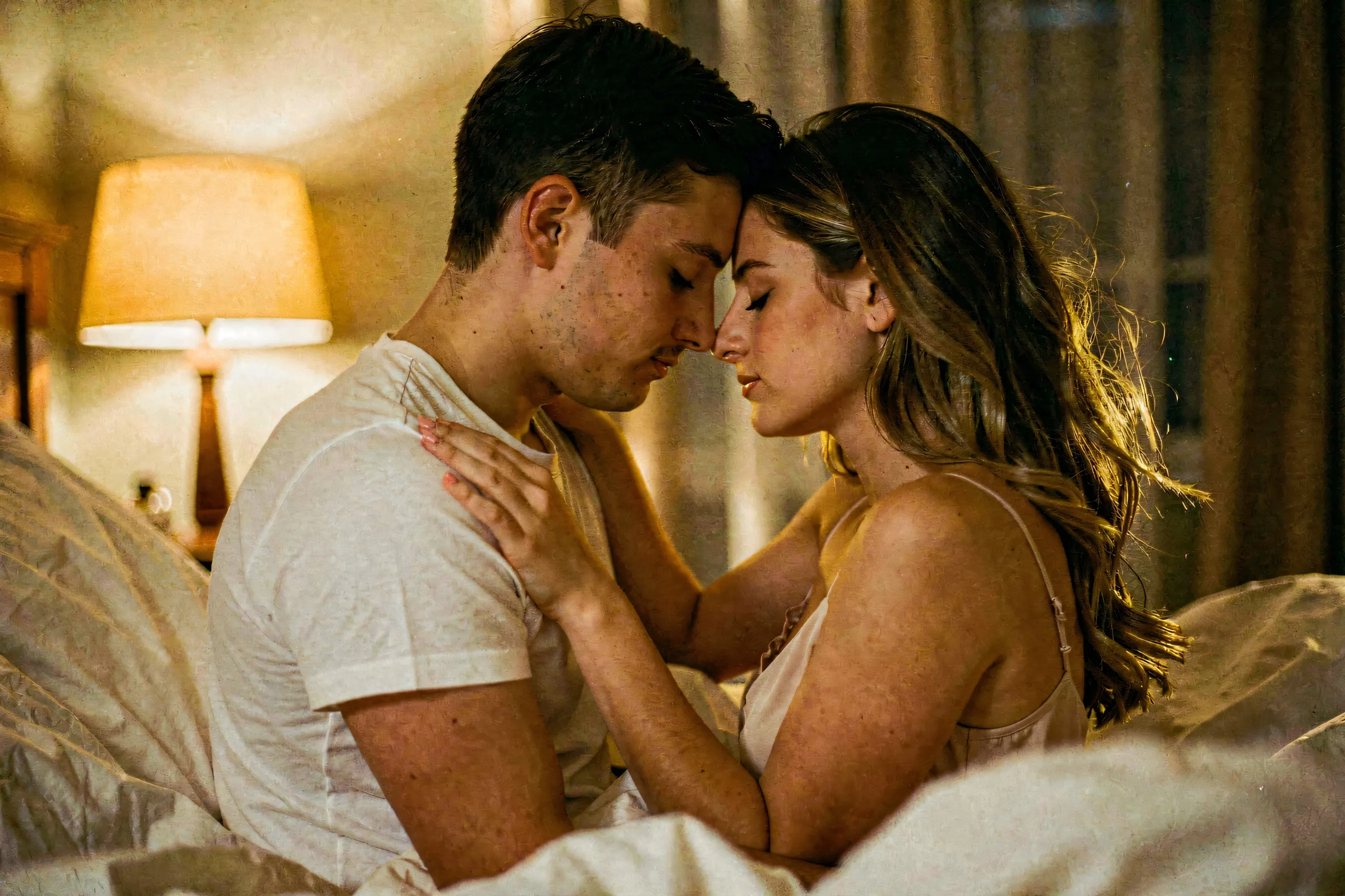A couple in a slow embrace, faces close, sheets mid-motion around them, golden lamplight