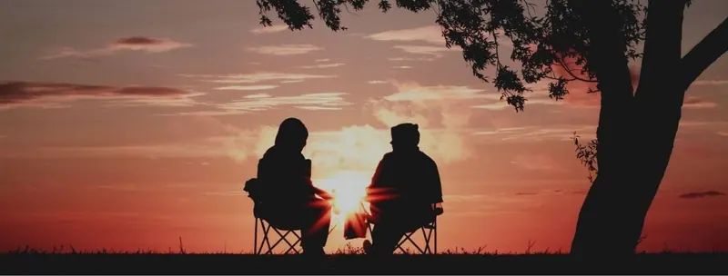 A couple sitting under a tree at dusk